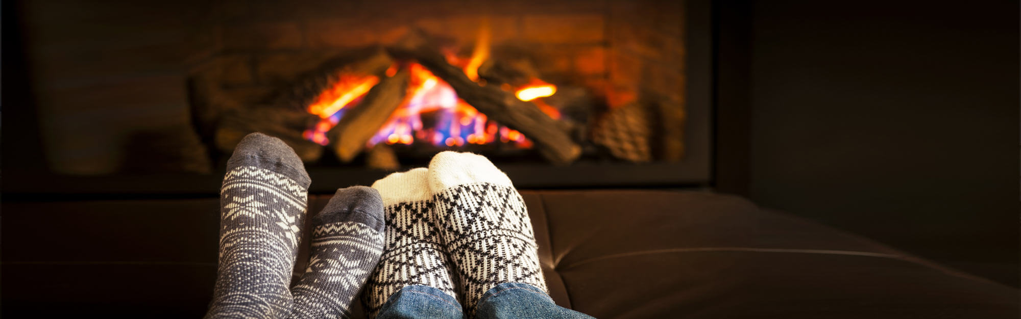 Two pairs of feet wearing warm winter socks warming in front of a fireplace